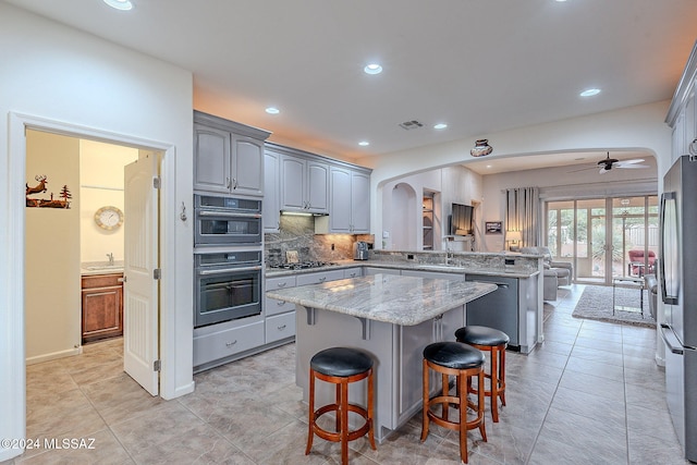 kitchen with gray cabinetry, backsplash, ceiling fan, appliances with stainless steel finishes, and a kitchen island