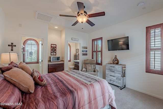 carpeted bedroom with multiple windows, ceiling fan, and ensuite bath