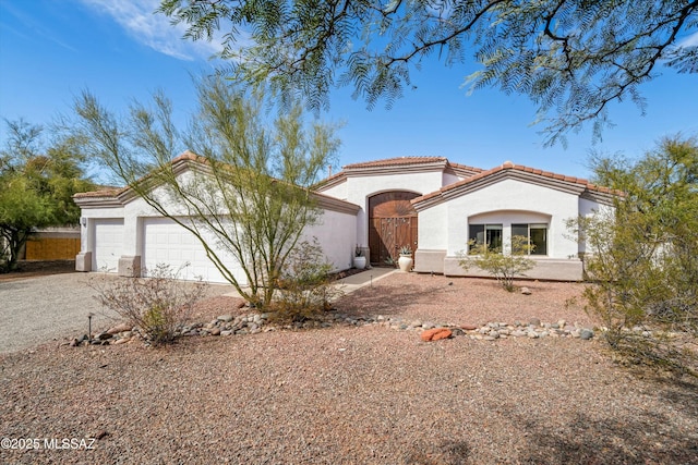 mediterranean / spanish-style house featuring a garage, a tiled roof, gravel driveway, and stucco siding