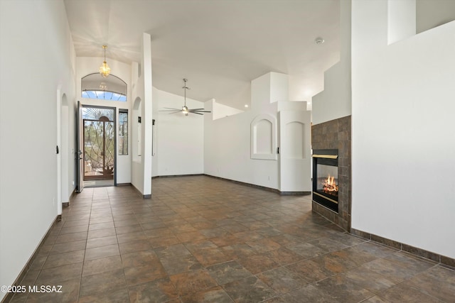 interior space with ceiling fan, high vaulted ceiling, a tile fireplace, and baseboards