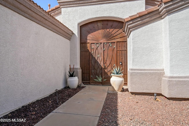 property entrance with a tile roof, a gate, and stucco siding