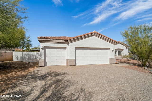 mediterranean / spanish home with a garage, gravel driveway, a tiled roof, and stucco siding