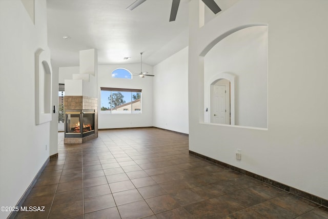 unfurnished living room featuring high vaulted ceiling, dark tile patterned flooring, a fireplace, a ceiling fan, and baseboards