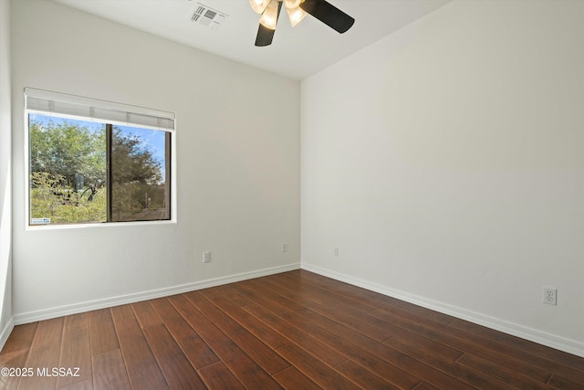 spare room with dark wood-type flooring, a ceiling fan, visible vents, and baseboards