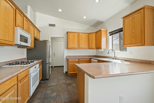 kitchen with white appliances, sink, vaulted ceiling, light brown cabinetry, and kitchen peninsula