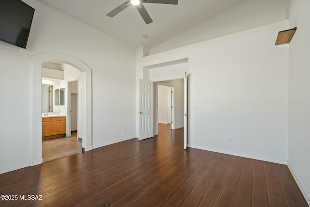 unfurnished bedroom featuring dark wood-type flooring, arched walkways, vaulted ceiling, and baseboards