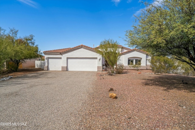 mediterranean / spanish-style home featuring gravel driveway, stucco siding, an attached garage, and a tiled roof