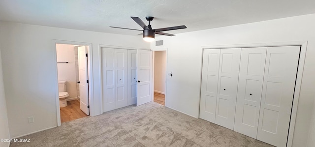 unfurnished bedroom with ensuite bathroom, light carpet, two closets, and ceiling fan