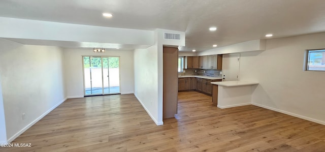 kitchen with kitchen peninsula, decorative backsplash, an inviting chandelier, and light wood-type flooring