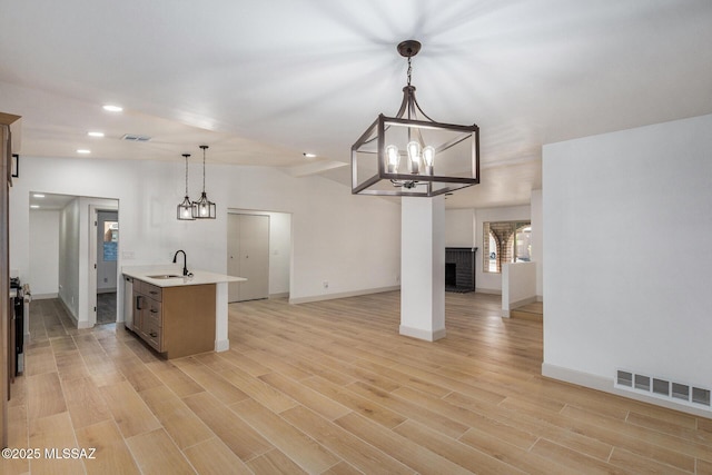 kitchen featuring sink, a brick fireplace, a center island with sink, light hardwood / wood-style flooring, and pendant lighting