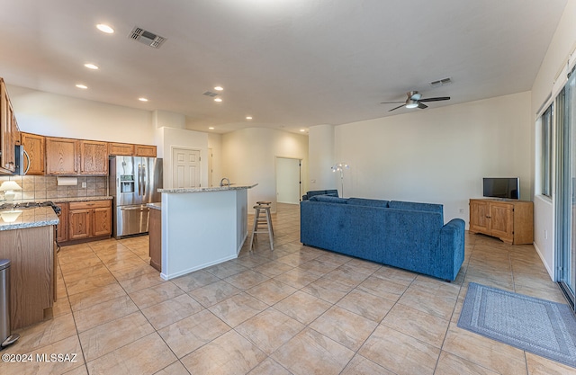 kitchen featuring ceiling fan, a kitchen island, backsplash, light stone countertops, and stainless steel appliances