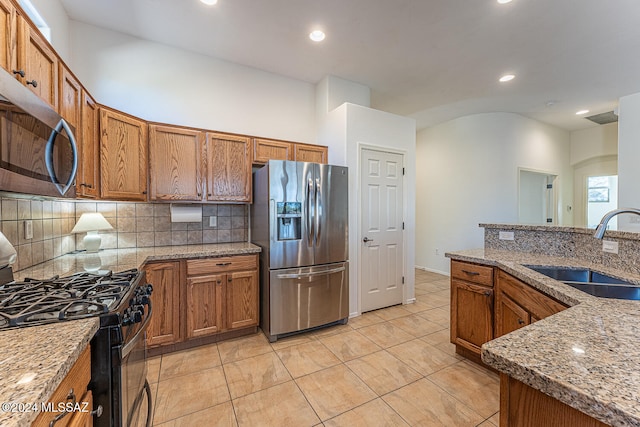 kitchen with sink, light tile patterned flooring, appliances with stainless steel finishes, light stone counters, and tasteful backsplash