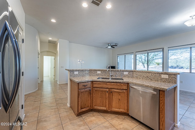 kitchen with ceiling fan, light stone countertops, a kitchen island with sink, stainless steel appliances, and sink