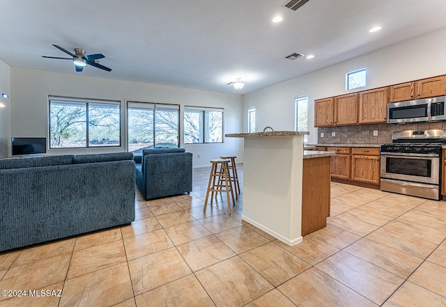 kitchen with backsplash, appliances with stainless steel finishes, plenty of natural light, and a kitchen bar