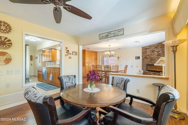 dining room featuring a fireplace, ceiling fan with notable chandelier, light hardwood / wood-style flooring, and sink