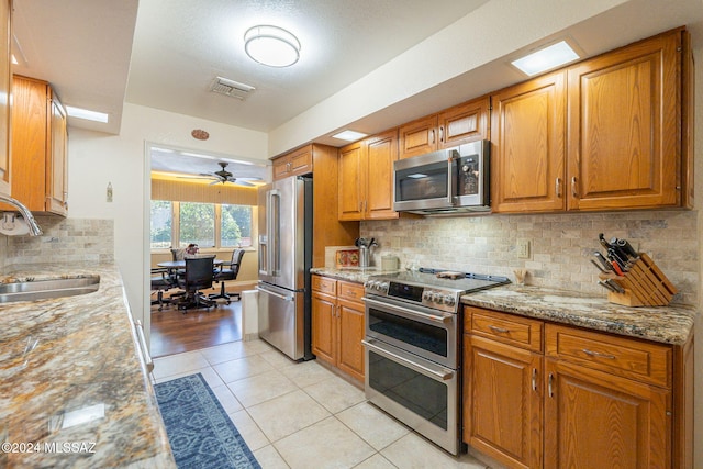 kitchen with light tile patterned floors, stainless steel appliances, tasteful backsplash, and ceiling fan