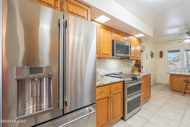 kitchen featuring ceiling fan, light stone countertops, appliances with stainless steel finishes, tasteful backsplash, and light tile patterned flooring