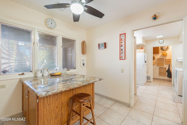 kitchen with ceiling fan, light stone counters, white refrigerator, washer / clothes dryer, and light tile patterned flooring