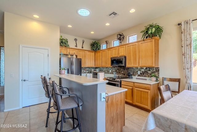 kitchen with tasteful backsplash, stainless steel appliances, a kitchen island, light tile patterned floors, and a kitchen breakfast bar