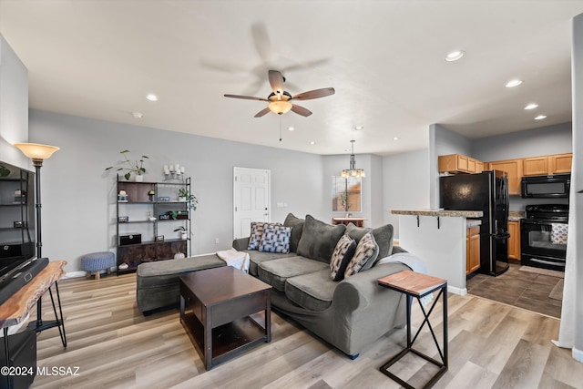 living room with light wood-type flooring and ceiling fan with notable chandelier