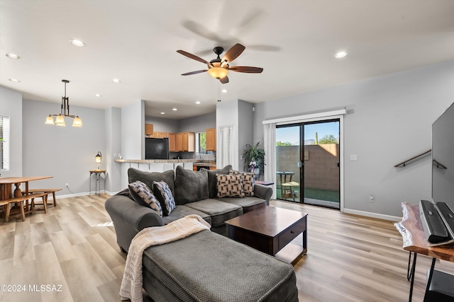 living room with ceiling fan with notable chandelier, sink, and light hardwood / wood-style flooring