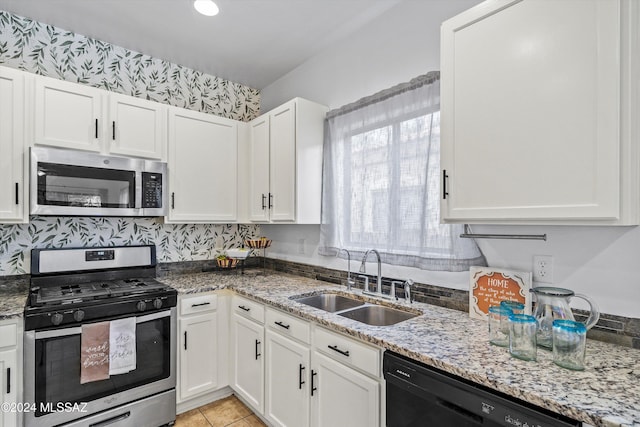 kitchen with sink, light tile patterned floors, appliances with stainless steel finishes, white cabinets, and light stone counters