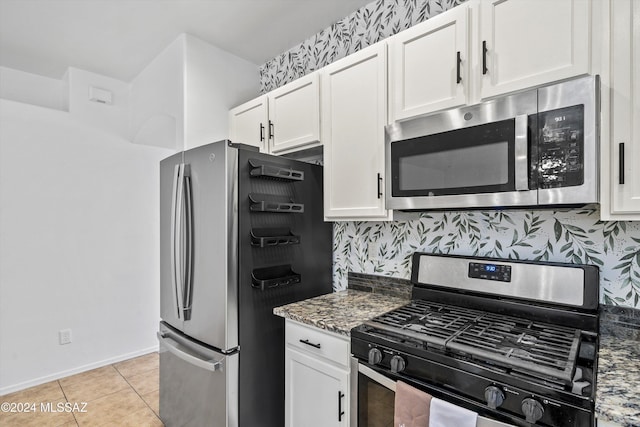 kitchen featuring appliances with stainless steel finishes, light tile patterned flooring, white cabinetry, dark stone counters, and tasteful backsplash