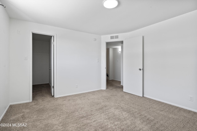 unfurnished bedroom featuring light colored carpet, a walk in closet, and a closet