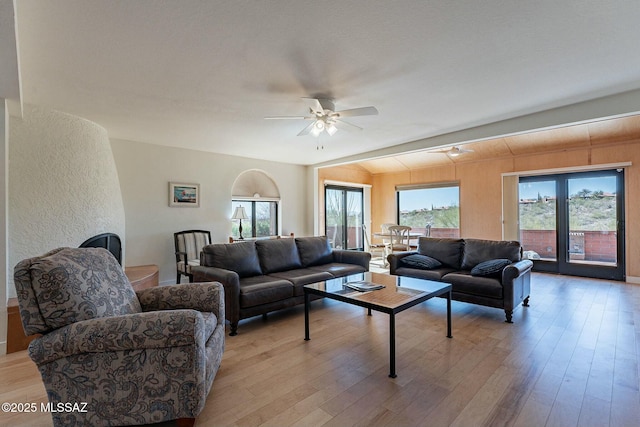 living area with lofted ceiling, light wood-style flooring, ceiling fan, and a textured wall