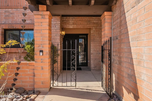 view of exterior entry featuring a gate and brick siding