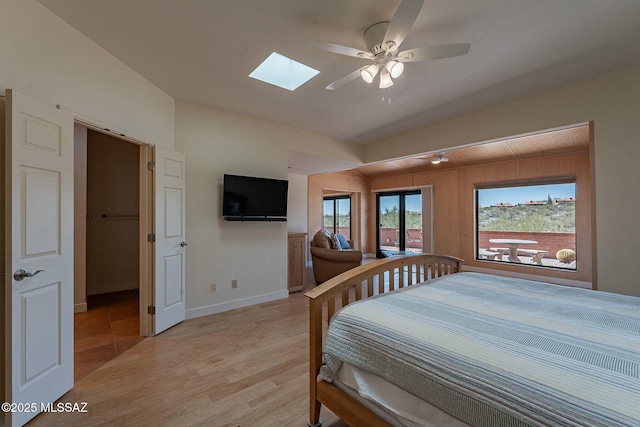 bedroom with vaulted ceiling with skylight, a ceiling fan, light wood-style flooring, and baseboards