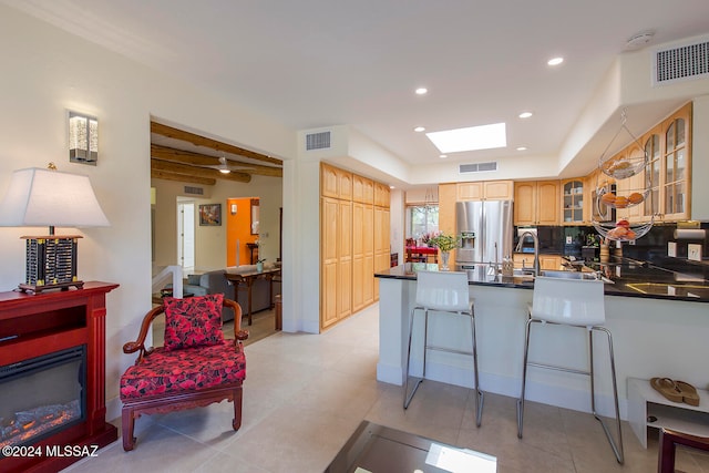 kitchen with kitchen peninsula, stainless steel refrigerator with ice dispenser, decorative backsplash, beamed ceiling, and a skylight