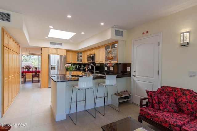 kitchen with kitchen peninsula, a kitchen bar, a skylight, and appliances with stainless steel finishes