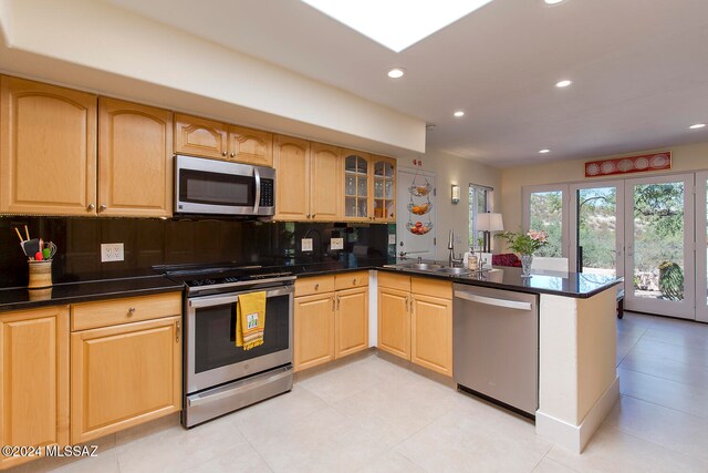 kitchen featuring stainless steel appliances, sink, kitchen peninsula, light brown cabinetry, and backsplash