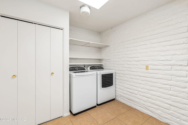 clothes washing area featuring washing machine and clothes dryer, light tile patterned floors, and brick wall