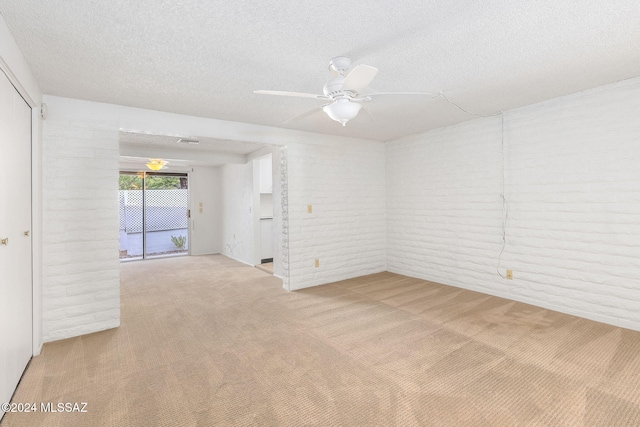 carpeted spare room featuring a textured ceiling, ceiling fan, and brick wall