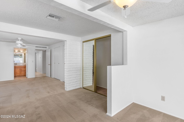 unfurnished bedroom with a textured ceiling, light colored carpet, ceiling fan, and a closet