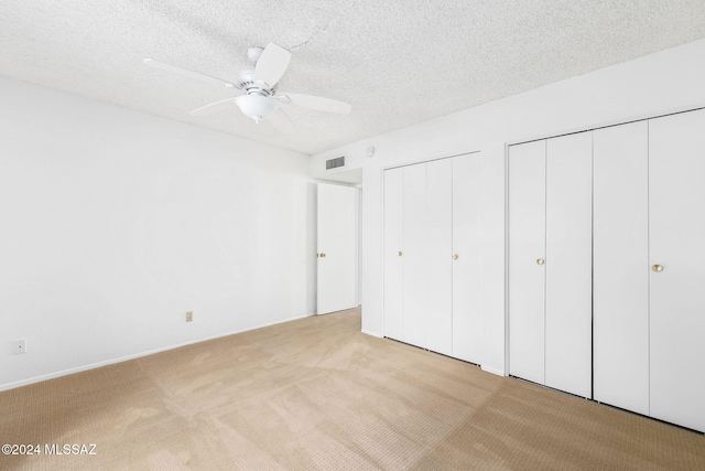 unfurnished bedroom featuring ceiling fan, a textured ceiling, light carpet, and multiple closets