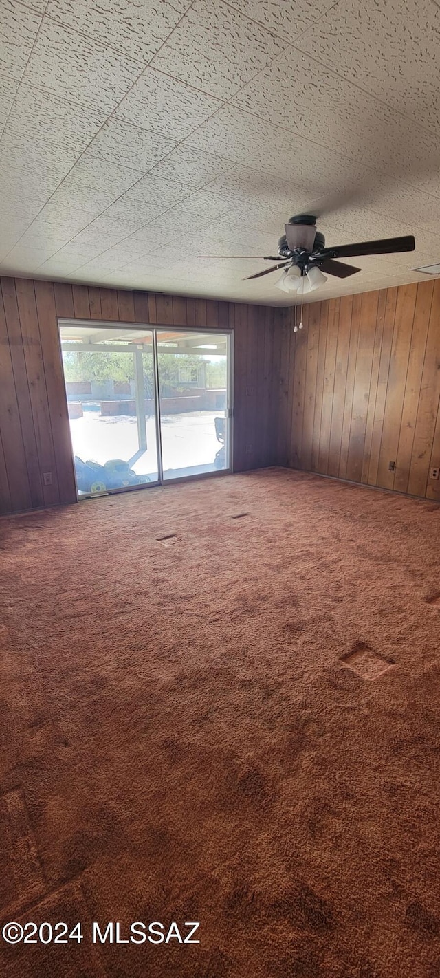 empty room with carpet floors, ceiling fan, and wooden walls