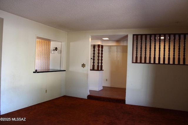 unfurnished room with a textured ceiling and dark colored carpet