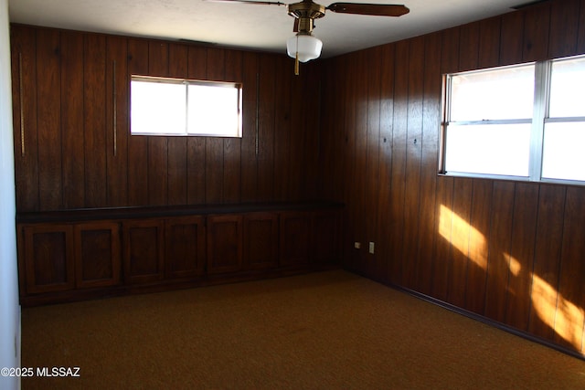 carpeted empty room with ceiling fan, a healthy amount of sunlight, and wood walls