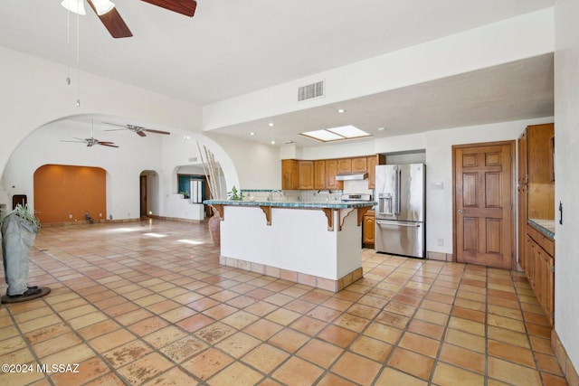 kitchen with a center island, stainless steel refrigerator with ice dispenser, decorative backsplash, a breakfast bar area, and light stone countertops