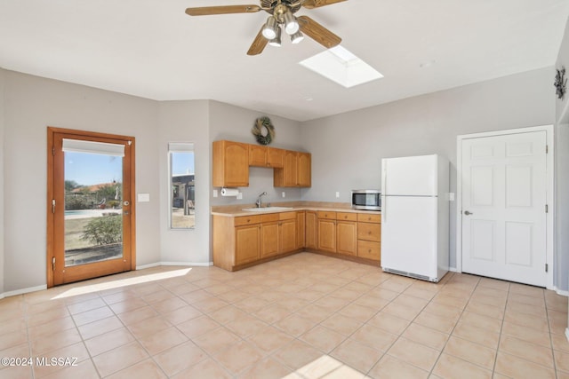 kitchen with light tile patterned floors, sink, ceiling fan, a skylight, and white fridge