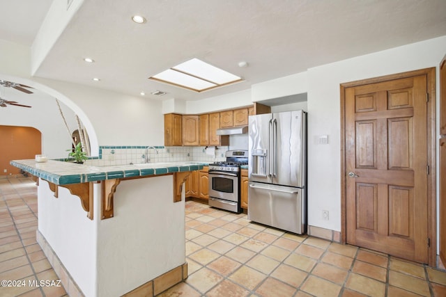 kitchen featuring light tile patterned flooring, appliances with stainless steel finishes, tasteful backsplash, a breakfast bar area, and tile counters