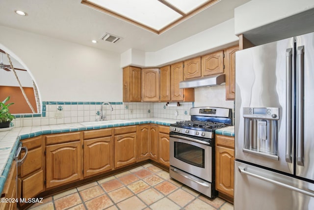 kitchen featuring stainless steel appliances, backsplash, sink, tile countertops, and ceiling fan