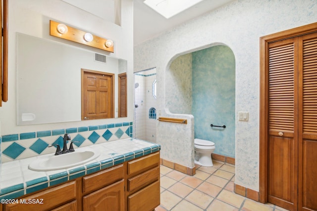 bathroom featuring toilet, tile patterned flooring, decorative backsplash, vanity, and a skylight