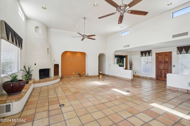 unfurnished living room featuring a high ceiling, ceiling fan, light tile patterned flooring, and a fireplace