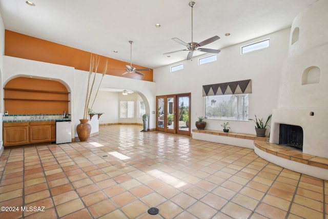 unfurnished living room featuring french doors, a towering ceiling, light tile patterned floors, a large fireplace, and ceiling fan