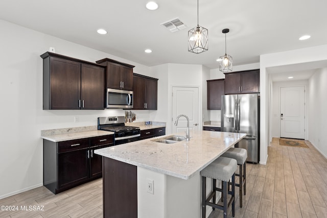 kitchen with a center island with sink, appliances with stainless steel finishes, dark brown cabinetry, sink, and light hardwood / wood-style flooring