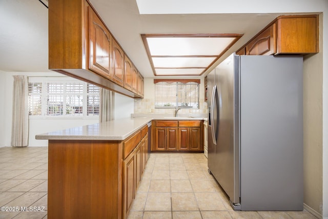 kitchen featuring light tile patterned flooring, sink, stainless steel fridge, kitchen peninsula, and backsplash